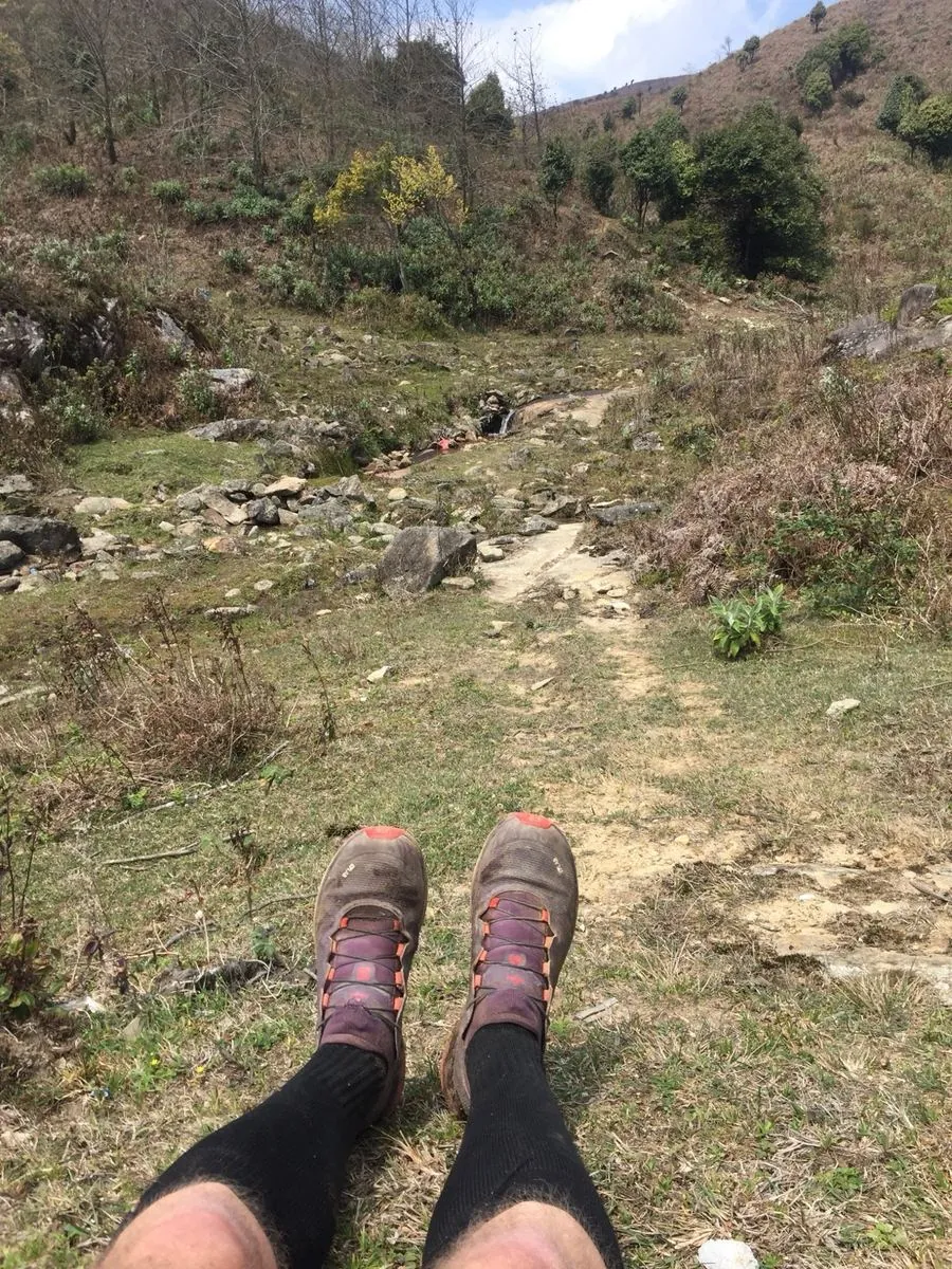 Benen met zwarte compressiekousen en trailschoenen tijdens een pauze op een bergpad.